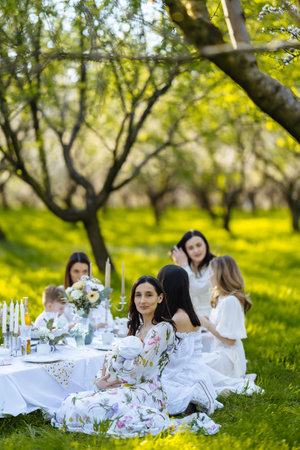 A group of several women are sitting around a table in a beautiful parkの写真素材