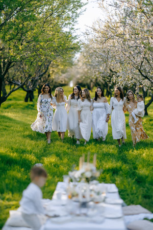 Women in white dresses stand around a table in a fieldの写真素材