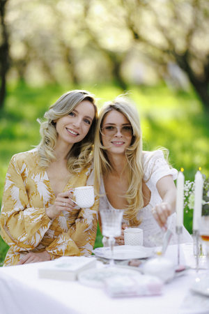 There are two women happily sitting at a table while holding cups of teaの写真素材