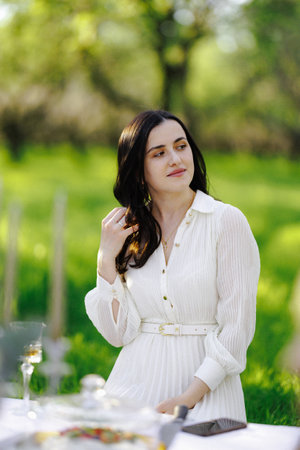 A woman in a beautiful white dress stands gracefully by a tableの写真素材
