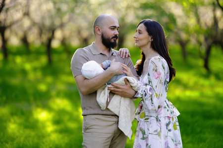 A man and woman are joyfully holding a cute baby in the parkの写真素材