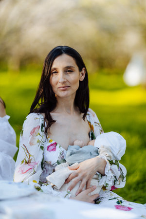 A woman is comfortably breastfeeding her baby in a lovely parkの写真素材