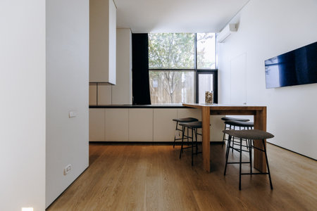 A cozy living room has a wooden table, stools, and a large windowの写真素材