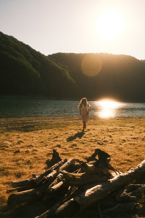 A woman is standing beside a large pile of logs near a lakeの写真素材