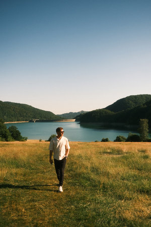 A man is walking through a serene field, with a lake behindの写真素材