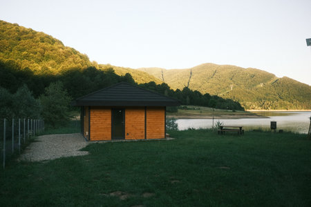 A small wooden house is in a grassy field next to a lakeの写真素材