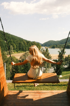 A woman is sitting on a swing that overlooks a beautiful lakeの写真素材