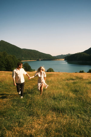 A man and woman hold hands walking in a field by a lakeの写真素材
