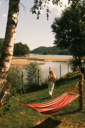 A woman stands by a hammock in front of a peaceful lakeの写真素材