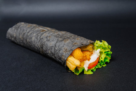 A black tortilla wrap with lettuce and chicken on black surfaceの写真素材