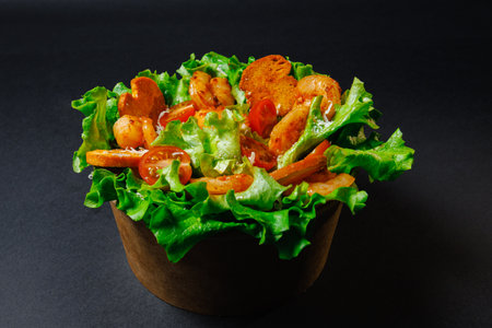 A salad with shrimp, fresh lettuce, and tomatoes in a wooden bowlの写真素材