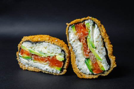 Two pieces of delicious sushi have been neatly cut in half on a black surfaceの写真素材