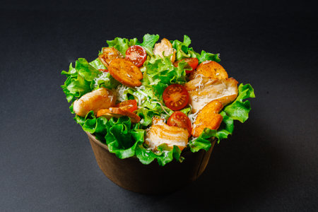 A bowl of salad with chicken, lettuce, and tomatoes on a tableの写真素材