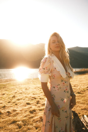 A woman in a floral dress stands on a beach at sunsetの写真素材