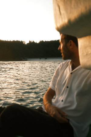 A man in a white shirt sits on a boat, looking at the waterの写真素材