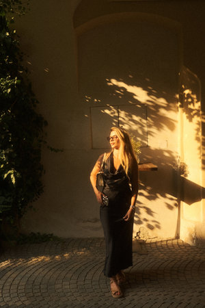 A woman in a stylish black dress stands confidently before a buildingの写真素材
