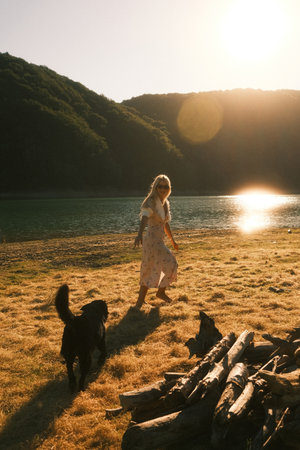 A woman is leisurely walking a dog along a beach by a lakeの写真素材