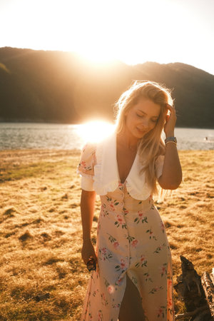 A woman in a floral dress stands on a beach at sunset, enjoying the viewの写真素材