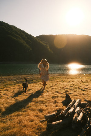A woman and a dog are joyfully running along a beach near a lakeの写真素材