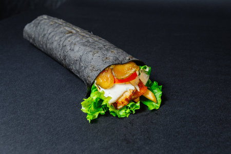 A black tortilla wrap with lettuce and chicken on black surfaceの写真素材