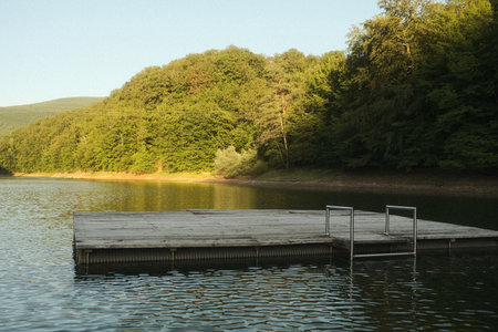 A dock sits in the center of a serene lake, bordered by treesの写真素材
