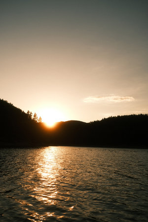 The sun sets over a serene lake with majestic mountains behindの写真素材