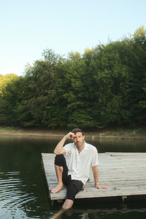 A man is peacefully sitting on a dock overlooking a serene lakeの写真素材