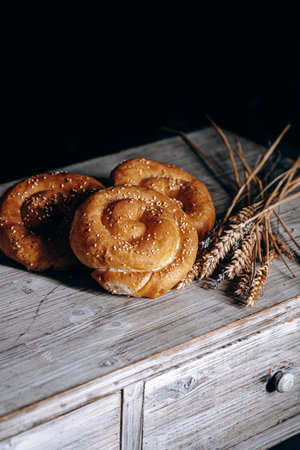 Indulge in Freshly Baked Rolls Adorned with Wheat Stalks on a Rustic Table Surfaceの写真素材