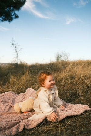 A Joyful Child Enjoying Playtime Outdoors with a Cozy Teddy Bear on a Colorful Blanketの写真素材