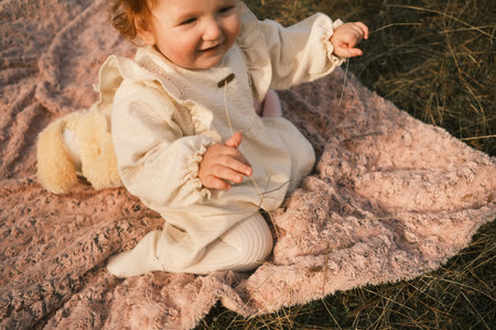 A Happy Baby is Sitting on a Soft and Pink Blanket Surrounded by Beautiful Natureの写真素材