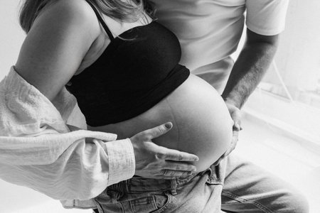 Pregnant woman peacefully embracing partner by window in softの写真素材