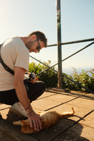 hiker bonding with ginger cat at coastal viewpointの写真素材