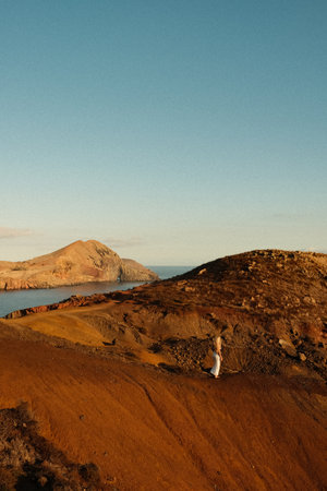 Lone female strolling along jagged red hills at dusk with oceanの写真素材