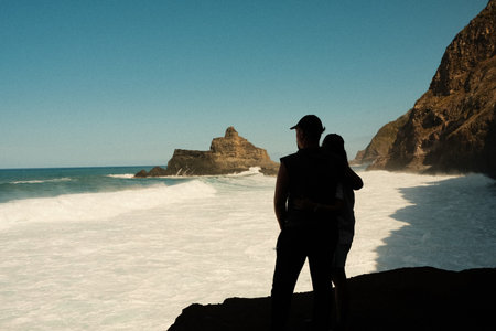 Intimate partners nestled on coastal stone amidst sunlightの写真素材