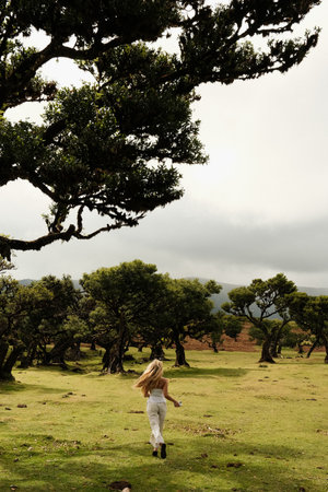 Woman wearing white moves freely through sunlit forest clearingの写真素材