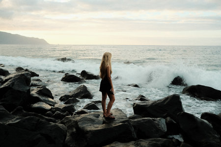 Caucasian woman poised on volcanic rocks facing turbulent oceanの写真素材