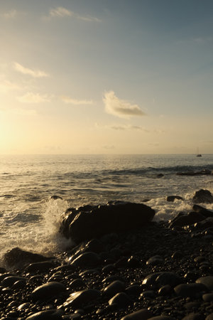 Golden light bathes dark stones along shoreline with reflectiveの写真素材