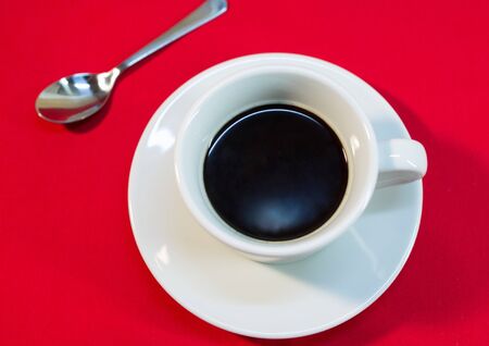 Top view of coffee spoon, saucer and white cup of black coffee on red tableclothの写真素材