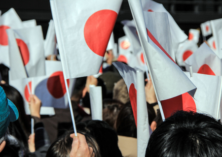 The crowd under the balcony in the square in front of the imperial palace on the first day of the New Year in Tokyo. People with national flags in the park.のeditorial素材