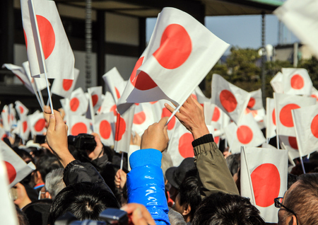 The crowd under the balcony in the square in front of the imperial palace on the first day of the New Year in Tokyo. People with national flags in the park.のeditorial素材
