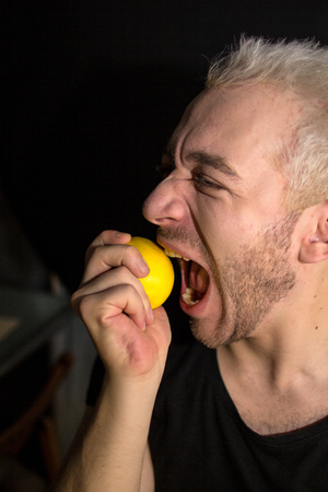 A portrait of a young bearded man. Funny guy biting lemon.の写真素材