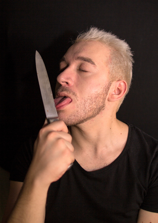 A portrait of a young bearded man. A man licking knife. Guy on black background.の写真素材