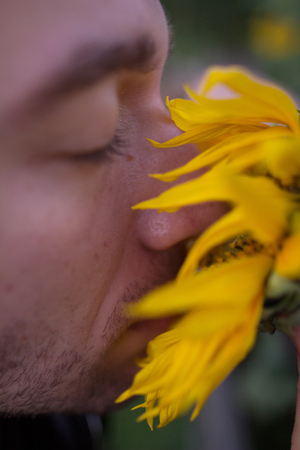 Close up portrait of a guy with a shut eyes and a sunflower by his face.の写真素材