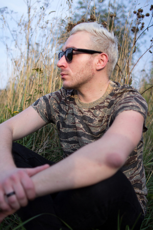 Portrait of a young attractive guy wearing a black sunglasses and sitting on a field.の写真素材