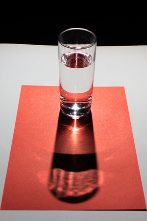 Glass of water on the red cardboard and white background. Abstract composition of colors and geometric figures.の写真素材
