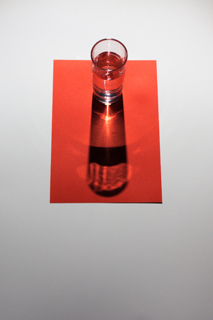 Glass of water on the red cardboard and white background. Abstract composition of colors and geometric figures.の写真素材