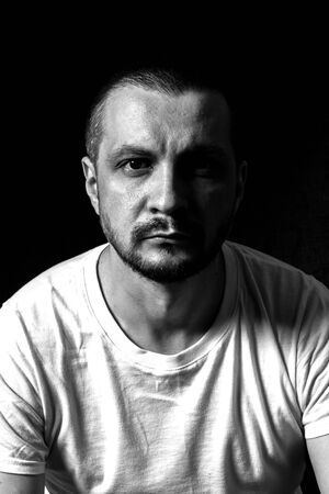 05/05/19, Moscow, Russia. Portrait of a young serious man sitting on black background and looking to...