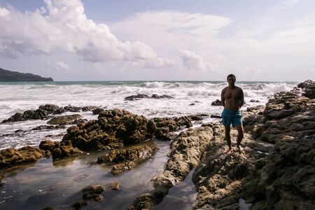 05.05.08, Phuket, Thailand. A young man standing on the rocks on background of ocean waves. Active tourism of Asia.の写真素材
