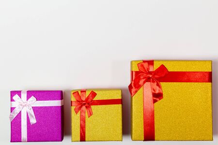 Three bright gift boxes with red ribbon on a white background. Concept of Happy birthday or another...