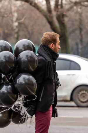 2015.11.22, Moscow, Russia. birthday is a sad holiday concept. A young blonde man wearing black scarf and coat guy holding black balloons and smoking.の写真素材